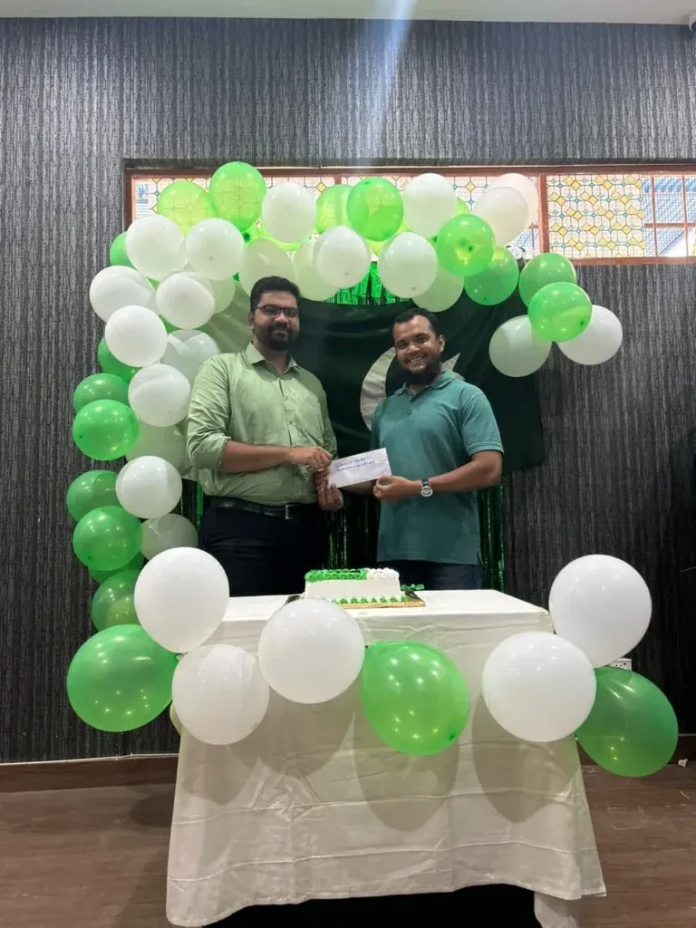 Two team members exchanging a gift beside the Independence Day cake, Sherdil 2023