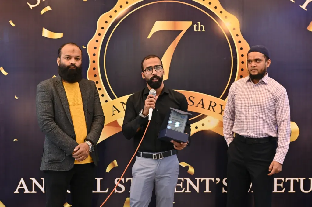 Alumnus speaking into a microphone while holding an award, Sherdil 7th anniversary 2024