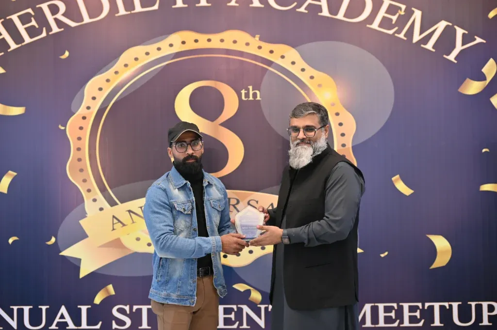 Award handover in front of the anniversary backdrop, Sherdil IT Academy 2025