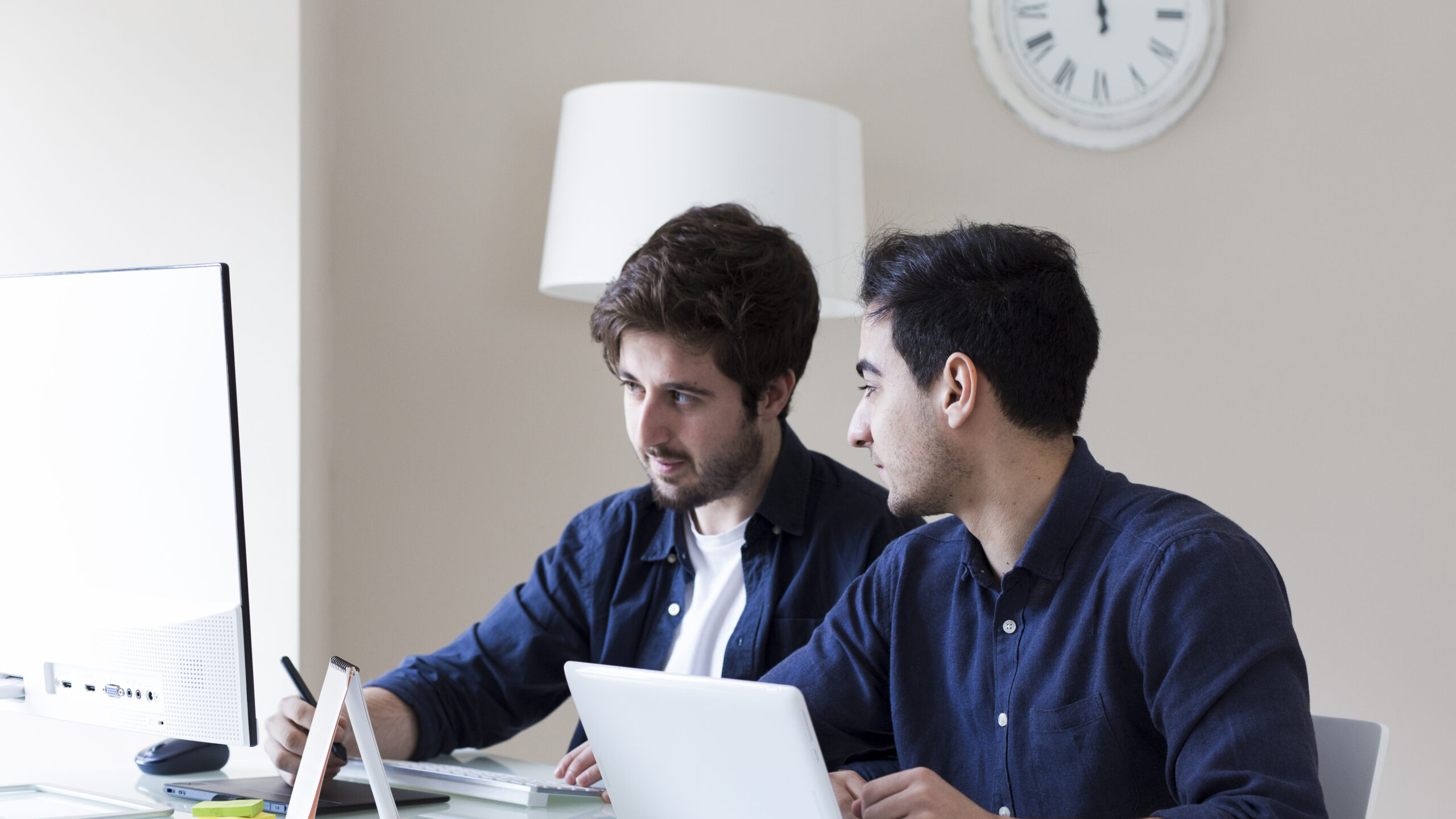 Two engineers comparing Kubernetes certification options (CKA vs CKAD) while studying on a computer.